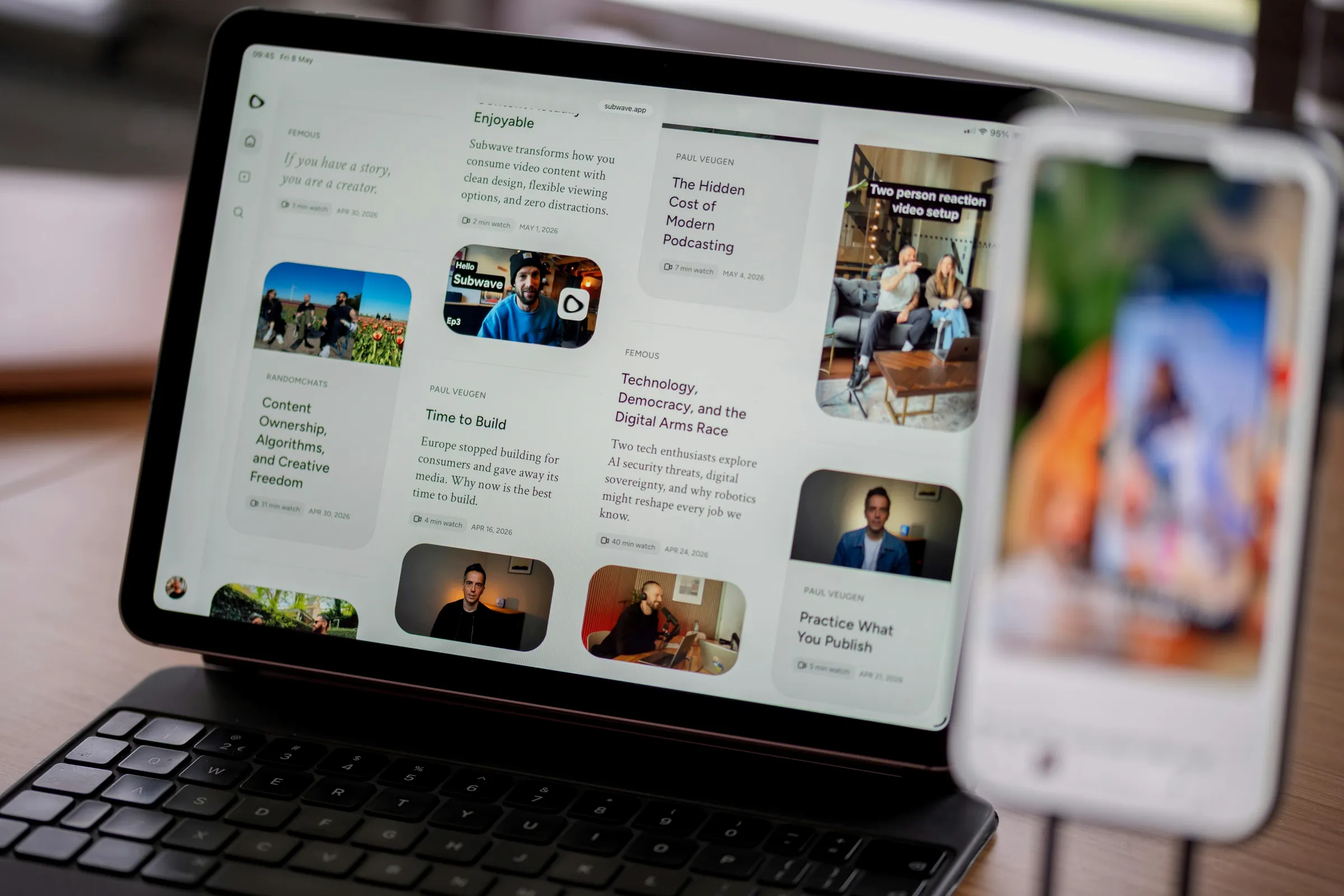 A tablet on a desk showing a video app, with a phone on a stand beside it.